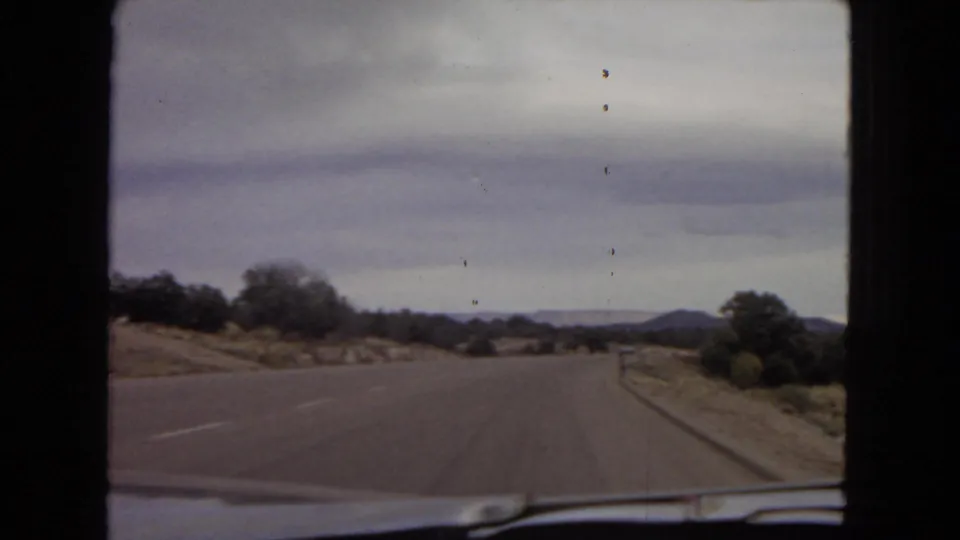 1967 Arizona road footage showing an empty paved roadway, roadside brush, distant hills, and a windshield edge from the car interior.