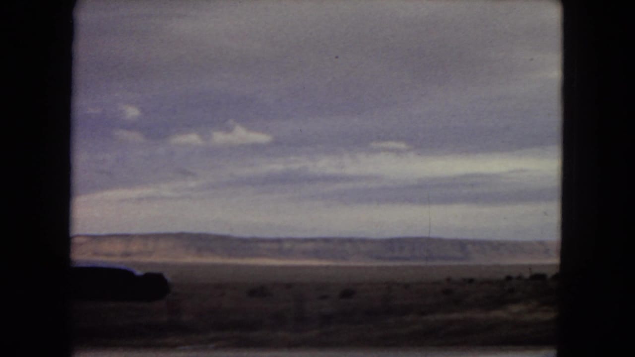 1967 Arizona road-trip footage appears to show an open desert plain and distant low mountains framed by the dark interior edges of a moving vehicle window.