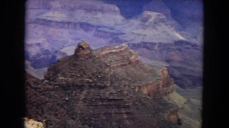 1967 8mm home-movie frame of a prominent Grand Canyon rock formation rising above layered canyon slopes and distant blue-toned cliffs.