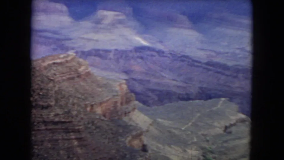 1967 8mm home-movie frame showing a wide Grand Canyon view with layered cliffs, blue distant walls, and pale canyon floor contours below.