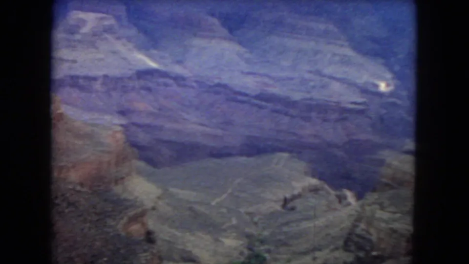 1967 8mm home-movie frame showing the Grand Canyon from above, with layered rock walls, deep ravines, and a purple-blue aged film cast.