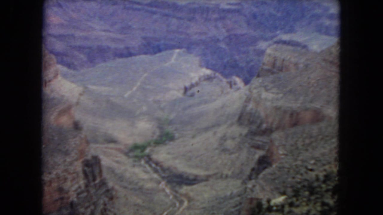 1967 8mm Arizona footage shows a soft, grainy view across Grand Canyon-like rock formations with a pale river or wash tracing the canyon floor.