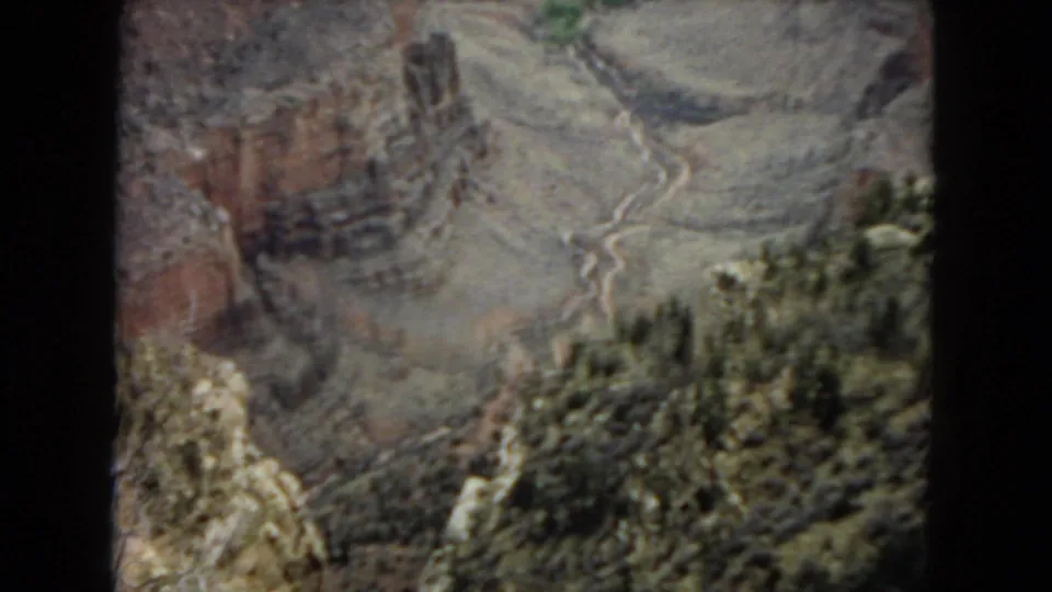 The 1967 8mm frame shows a slightly closer canyon view with a prominent rock face, pale drainage line, and darker shrubs or trees near the lower edge.