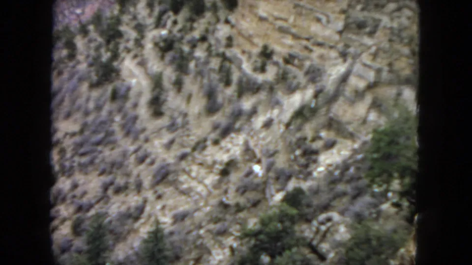 1967 Arizona desert frame showing rough rocky ground, winding dry gullies, sparse shrubs, and soft 8mm texture during the pan.