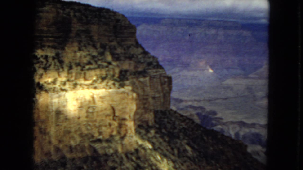 1967 Arizona 8mm frame showing sunlight breaking across a canyon wall, with darker blue-purple canyon depth in the background and film-gate edges visible.