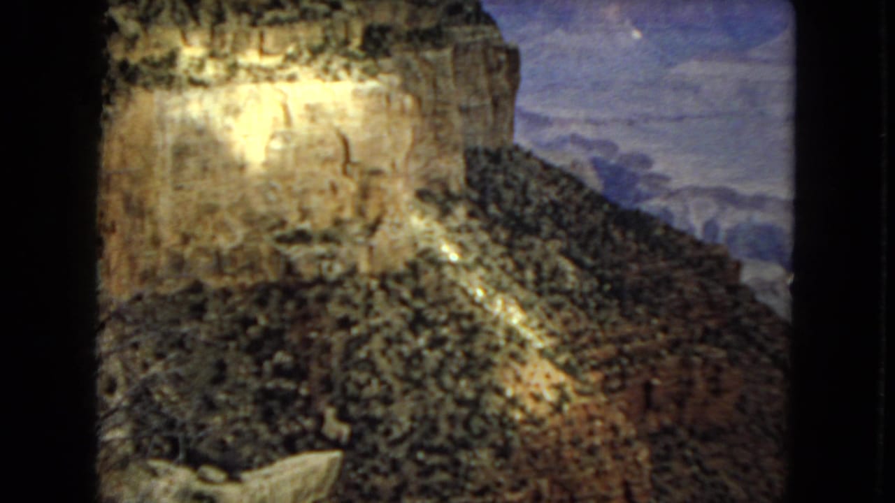 1967 Arizona 8mm frame of a high canyon face and rocky slope, with a concentrated shaft of sunlight against darker overcast canyon shadows.