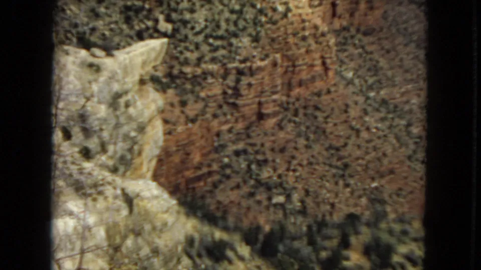 1967 Arizona 8mm frame of layered canyon rock, pale foreground stone, reddish cliff texture, and a darker ravine area near the bottom of the frame.