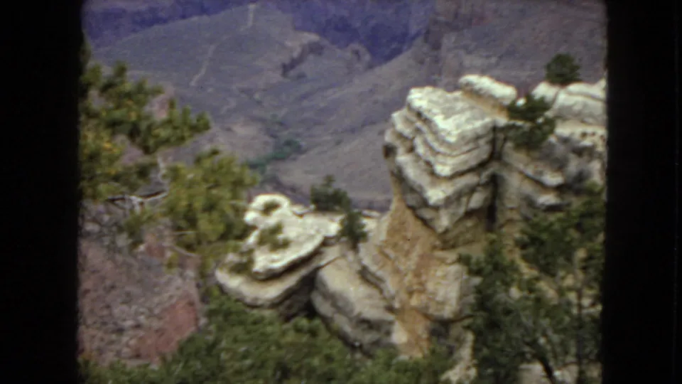 1967 Arizona 8mm frame showing a rocky overlook with scrub vegetation, pale stratified stone, and a steep canyon wall descending in the background.