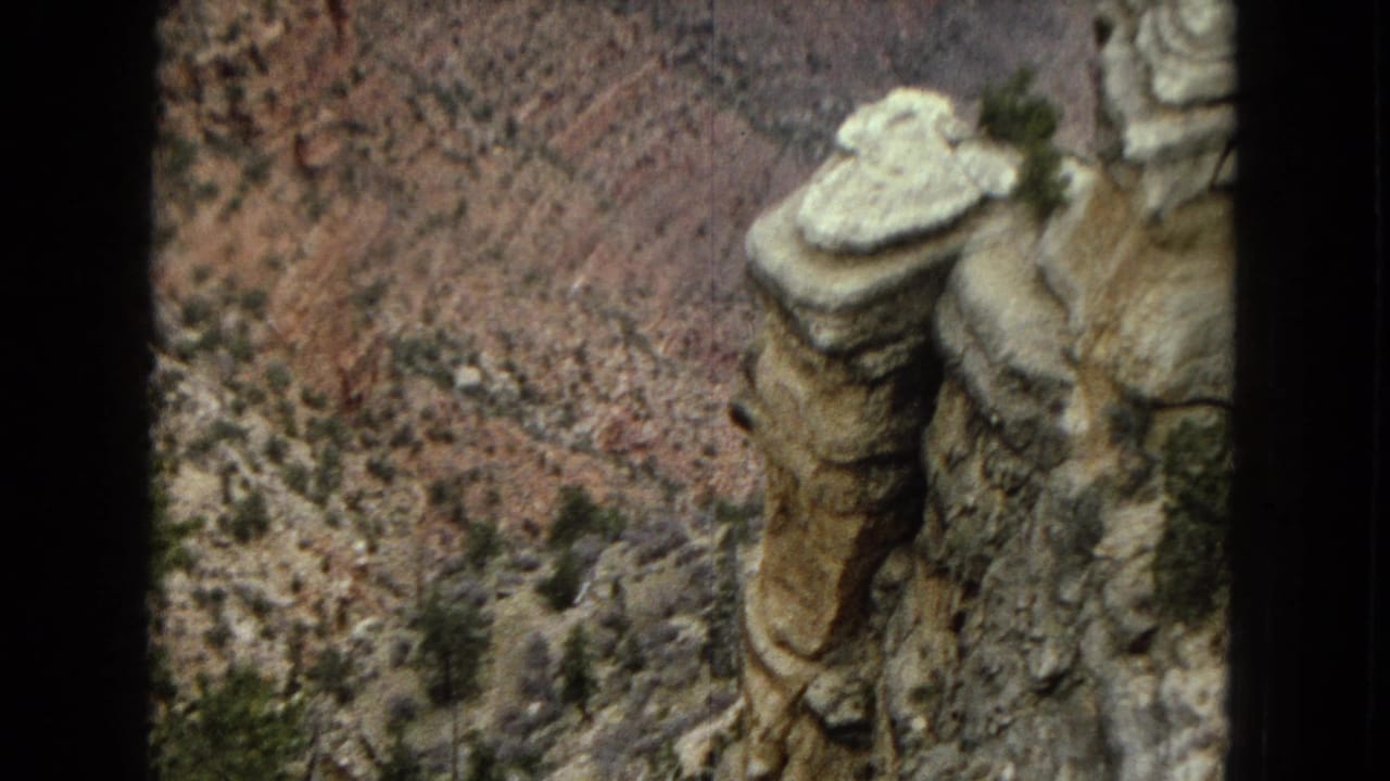 1967 Arizona 8mm frame with a tall pale rock column and steep Grand Canyon terrain behind it.