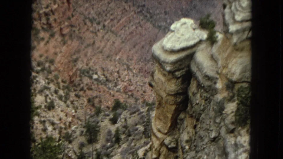 1967 Arizona 8mm frame with a tall pale rock column and steep Grand Canyon terrain behind it.