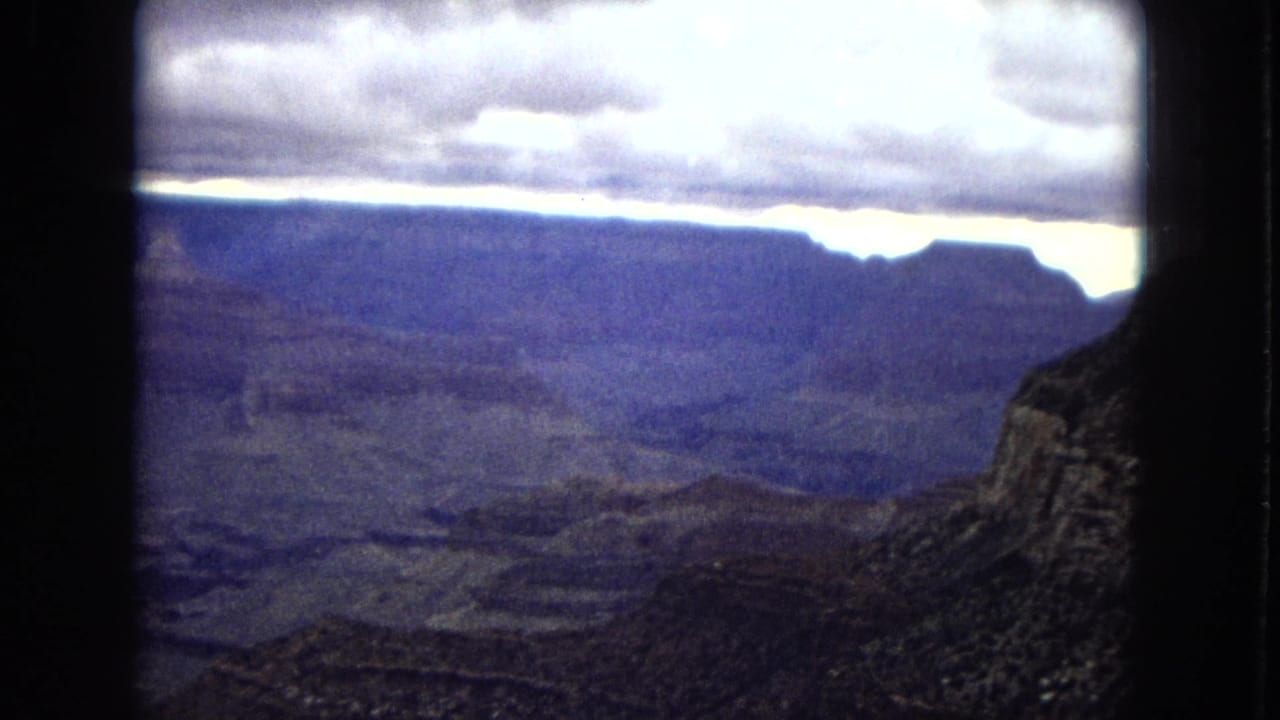Wide canyon view with dark plateau silhouettes and a bright strip of sky below heavy clouds.