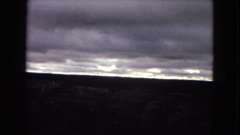 1967 Arizona 8mm view of a heavy cloud ceiling and glowing horizon line, with dark foreground dividers suggesting the scene was filmed through a window or structural opening.