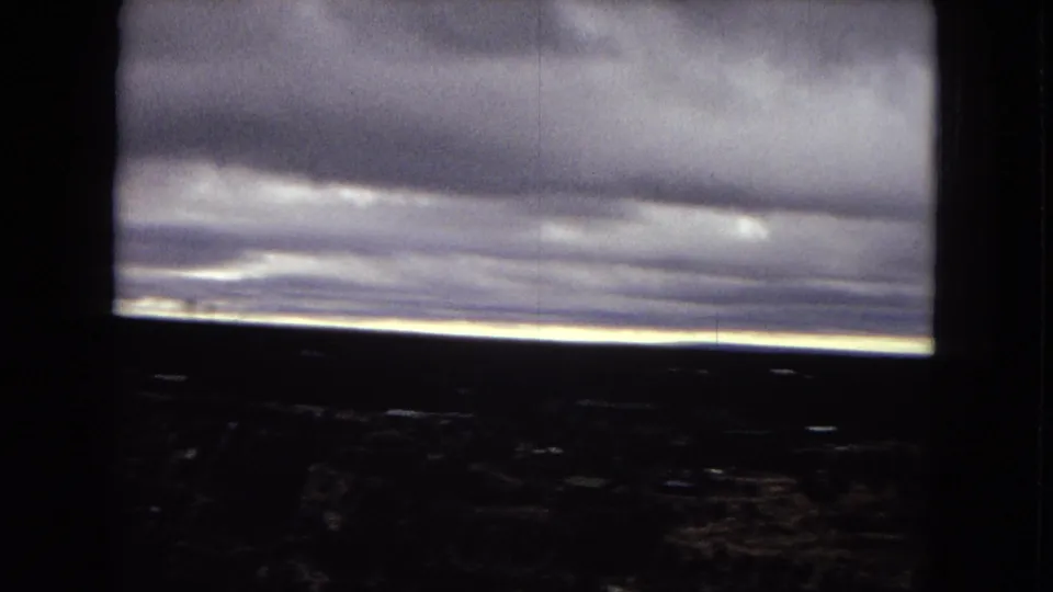 1967 Arizona 8mm frame showing a long bright horizon below dense clouds, with dark foreground terrain and vertical film marks visible in the scanned image.