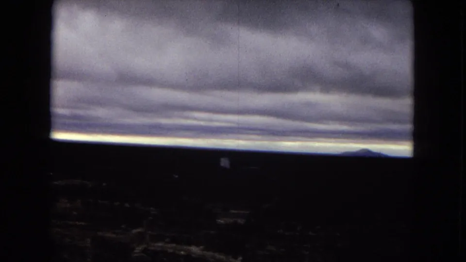 A moody overcast sky hangs above the distant Grand Canyon rim in vintage 8mm footage, with most landforms held in shadow.
