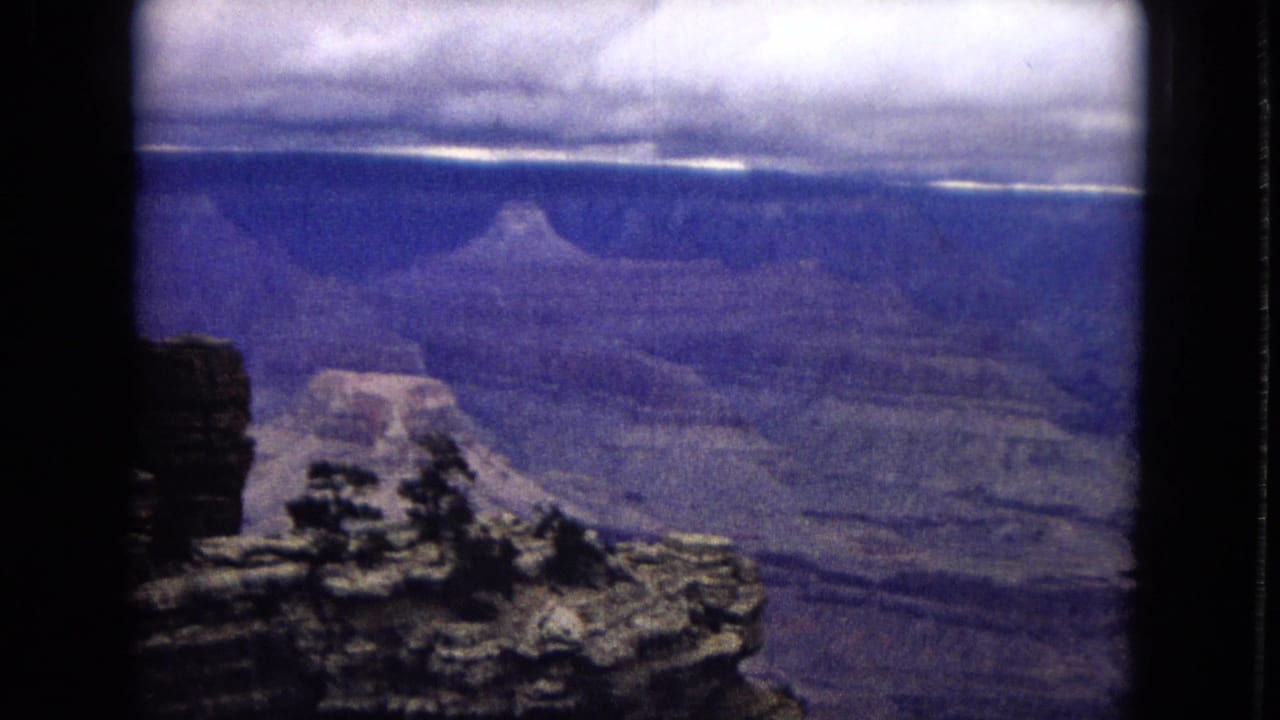 1967 Arizona 8mm home-movie frame looking from a rocky Grand Canyon overlook toward layered canyon walls and a clouded horizon.