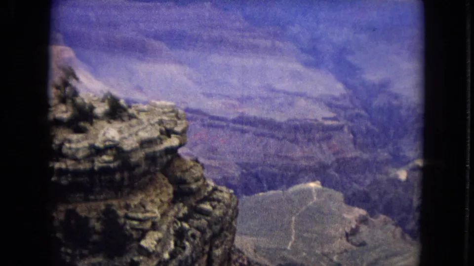 1967 Arizona 8mm frame showing a rugged rock outcrop above the Grand Canyon with distant ridges and a broad basin below.