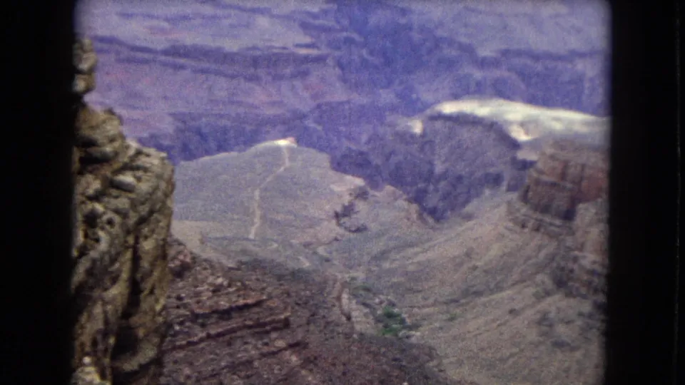 1967 Arizona 8mm home-movie frame looking down across steep Grand Canyon walls, pale slopes, and rugged rock formations.