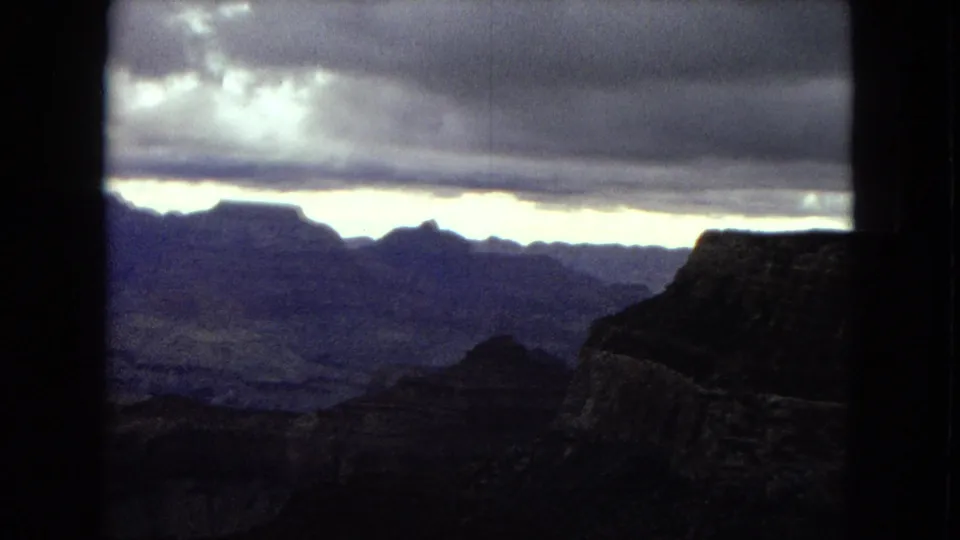 1967 Arizona 8mm frame with the Grand Canyon in dark silhouette beneath heavy clouds and a narrow bright break along the horizon.
