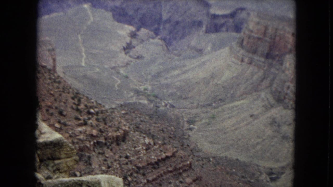 1967 8mm view of the Grand Canyon from above, showing layered rock walls, a deep basin, and soft faded home-movie color.