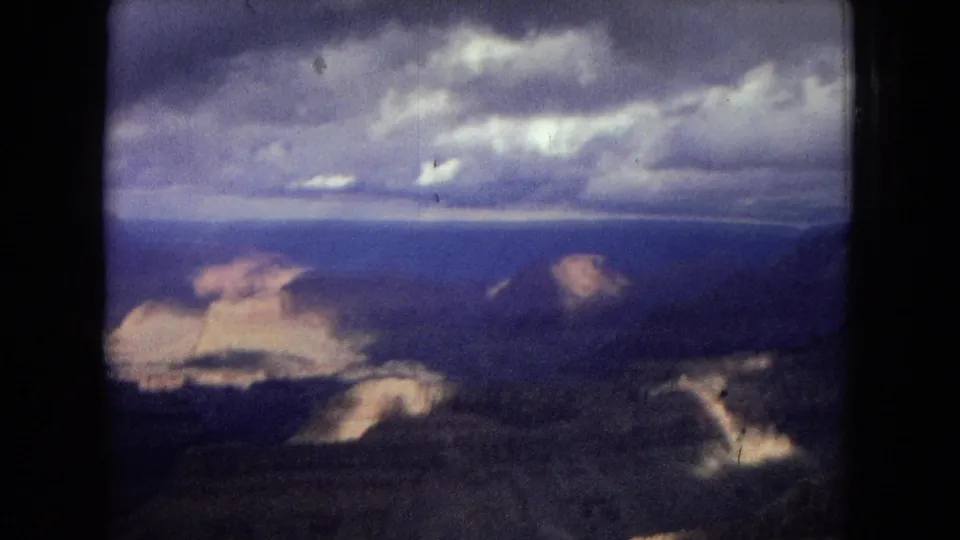 Vintage 8mm frame from the Grand Canyon showing a broad canyon vista, distant horizon, and heavy clouds with visible film softness and color shift.