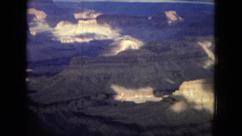 1967 8mm home-movie frame showing layered Grand Canyon rock walls, bright sunlit stone patches, and dark canyon recesses under clouded light.