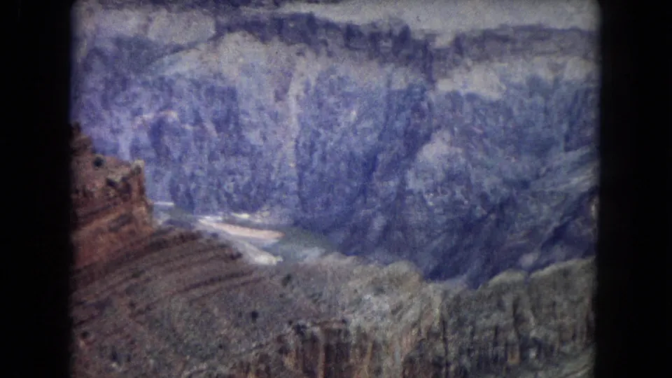 1967 8mm frame of Grand Canyon strata and eroded formations, with a small pale river channel visible through the lower valley.