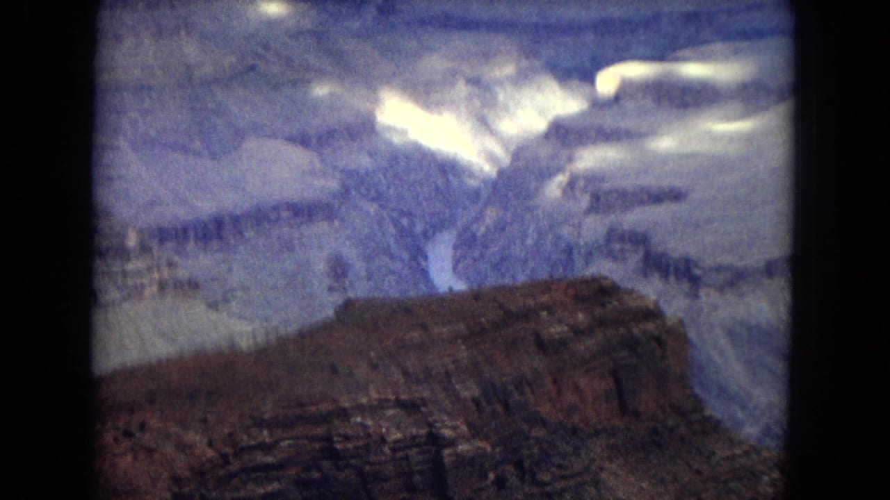 1967 8mm view across the Grand Canyon with a foreground plateau, distant river channel, and soft cloud light over the canyon walls.