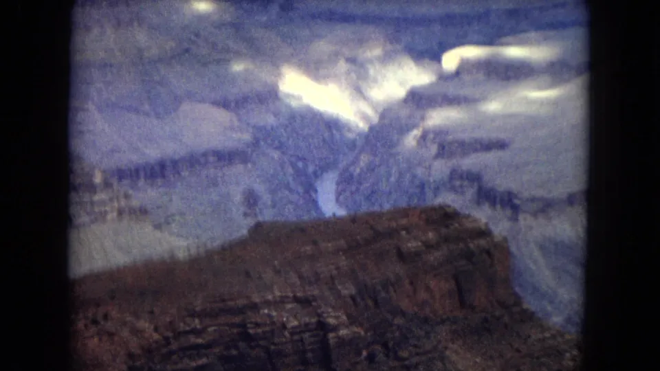 1967 8mm view across the Grand Canyon with a foreground plateau, distant river channel, and soft cloud light over the canyon walls.