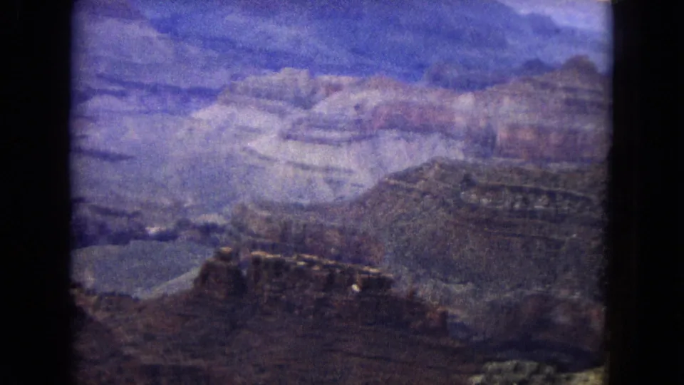 1967 Arizona landscape frame showing a soft, grainy Grand Canyon view with mesas, layered rock, shadowed ravines, and blue sky broken by clouds.