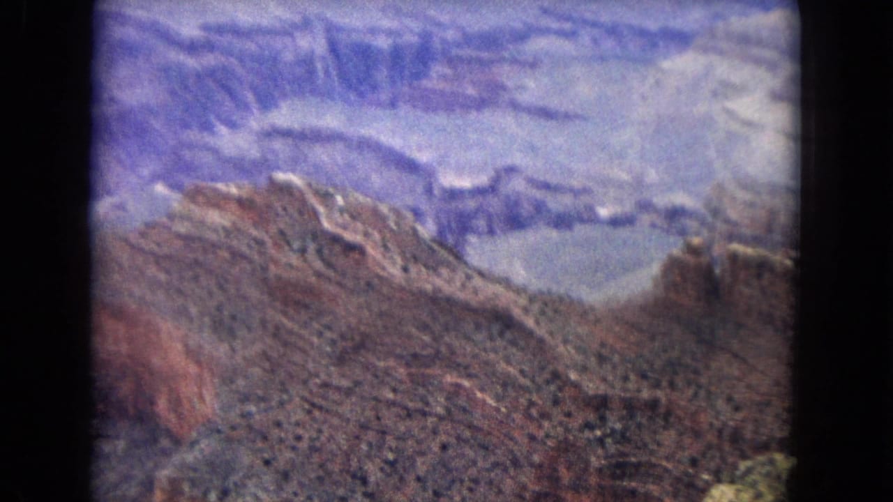 1967 Arizona 8mm view across a rocky Grand Canyon ridge with deep ravines and pale stratified cliffs in the distance.