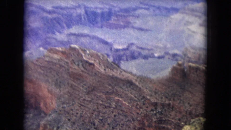 1967 Arizona 8mm view across a rocky Grand Canyon ridge with deep ravines and pale stratified cliffs in the distance.