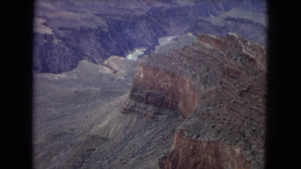 1967 Arizona home-movie view across a deep canyon basin with a reddish ridge, pale rock shelves, and blue shadowed depths.