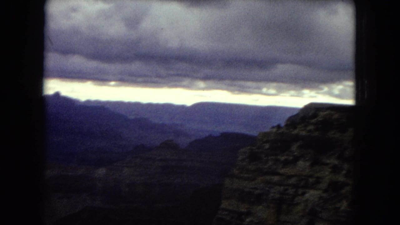 1967 8mm home-movie frame showing a shadowed Grand Canyon overlook beneath heavy clouds and a pale dusk horizon.
