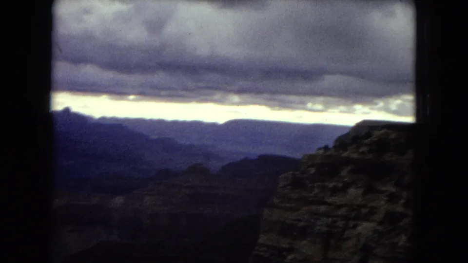 1967 8mm home-movie frame showing a shadowed Grand Canyon overlook beneath heavy clouds and a pale dusk horizon.