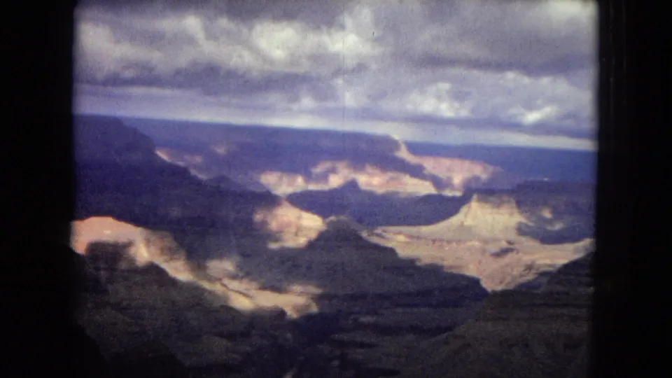 Aerial Grand Canyon view from 1967 8mm footage, showing bright canyon walls, dark ridges, distant horizon, and visible film-frame edges.