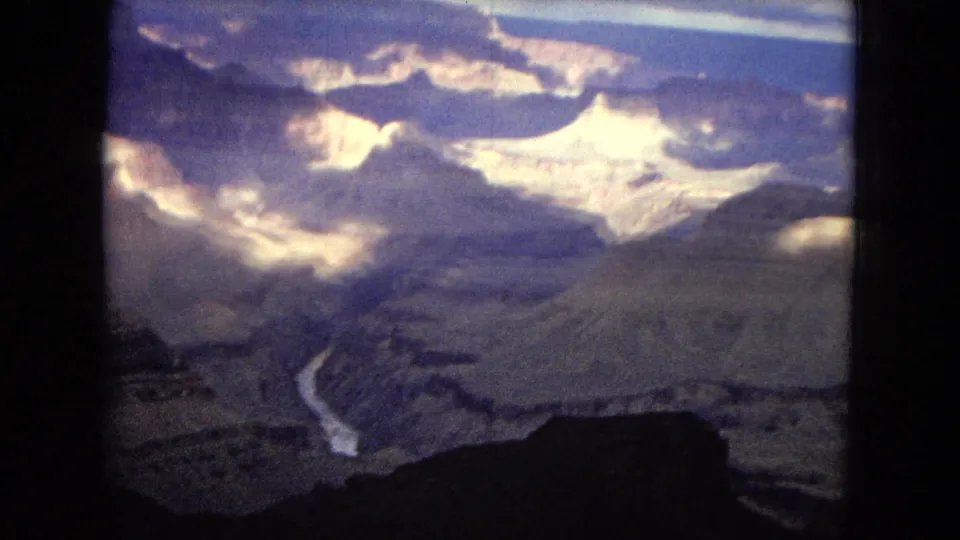 Final aerial frame of the 1967 Grand Canyon footage, with a winding river below, broad canyon walls, heavy cloud shadows, and dark film-edge framing.
