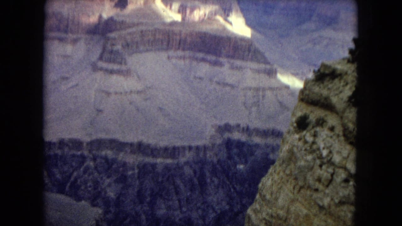 1967 Arizona 8mm home-movie view of layered Grand Canyon cliffs, with a dark overlook edge framing distant sunlit rock formations.