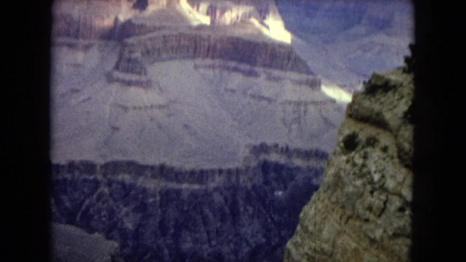 1967 Arizona 8mm home-movie view of layered Grand Canyon cliffs, with a dark overlook edge framing distant sunlit rock formations.