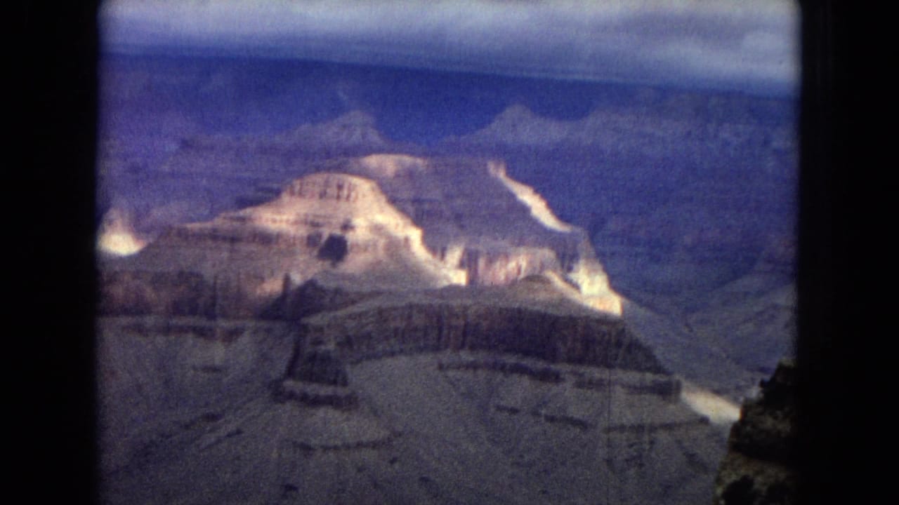 1967 Arizona 8mm view across the Grand Canyon, showing a bright cliff formation, distant rim layers, and a partly clouded blue sky.