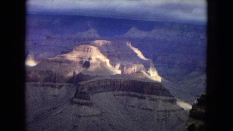 1967 Arizona 8mm view across the Grand Canyon, showing a bright cliff formation, distant rim layers, and a partly clouded blue sky.