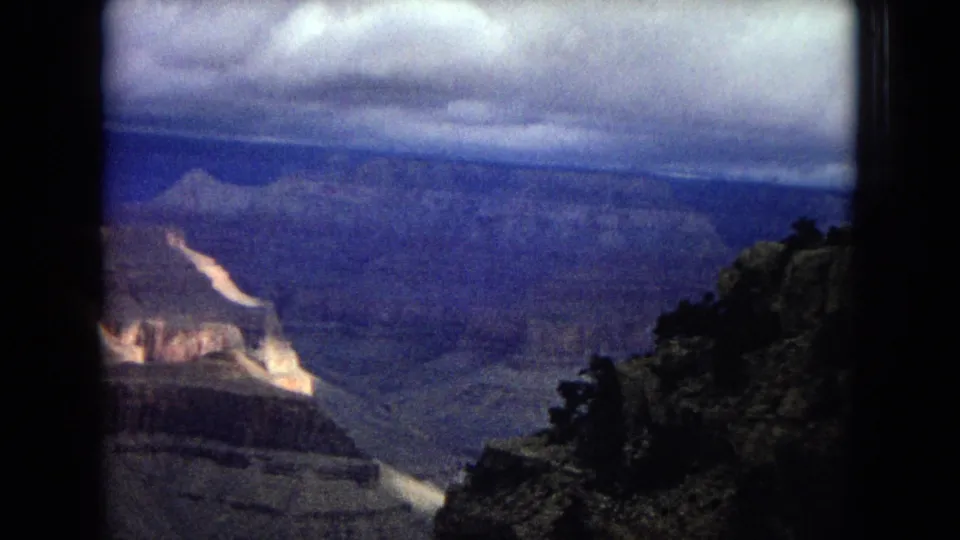 1967 Arizona 8mm home-movie frame from a Grand Canyon overlook, with dark trees in the foreground and layered canyon walls receding into the distance.