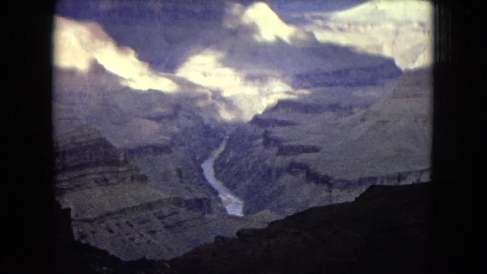 1967 Arizona 8mm view into the Grand Canyon, showing bright cliff faces, shadowed rock layers, and the Colorado River winding through the canyon floor.