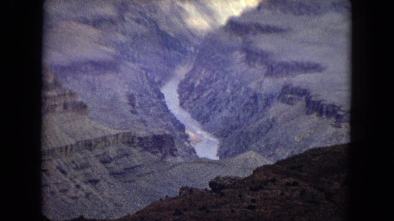 1967 8mm canyon panorama showing the Colorado River between steep striated Grand Canyon walls with a dark foreground slope.