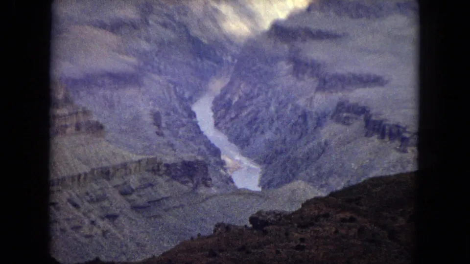 1967 8mm canyon panorama showing the Colorado River between steep striated Grand Canyon walls with a dark foreground slope.