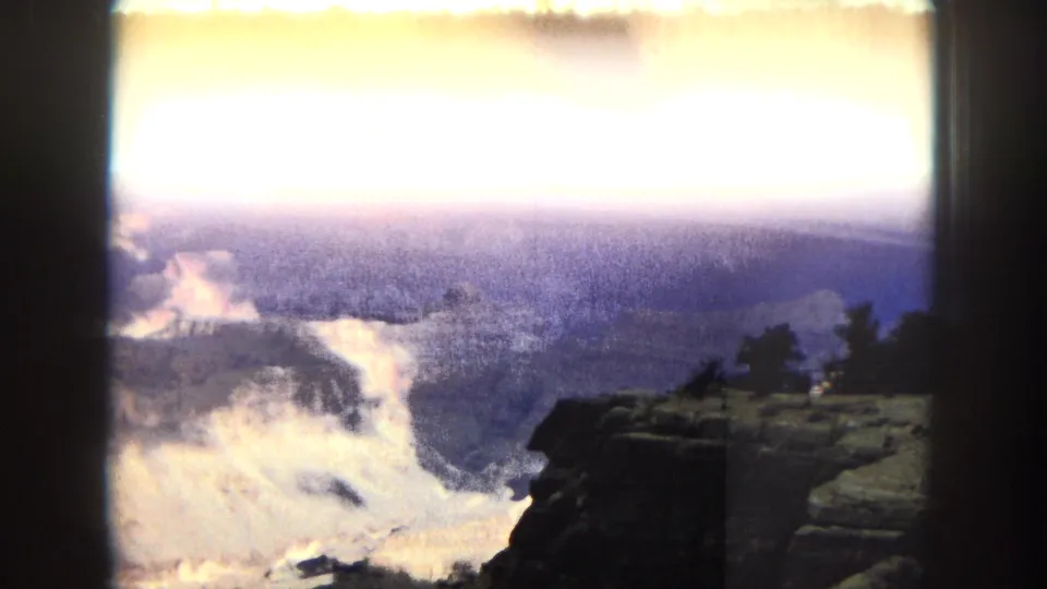 1967 8mm Grand Canyon overlook view with a bright exposed sky, river bend below, and a dark cliff edge in the foreground.