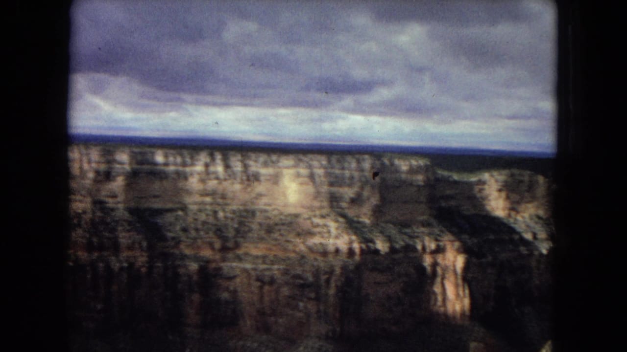 1967 8mm home-movie frame showing broad Grand Canyon cliffs, dark canyon shadows, and a low band of stormy cloud above the rim.