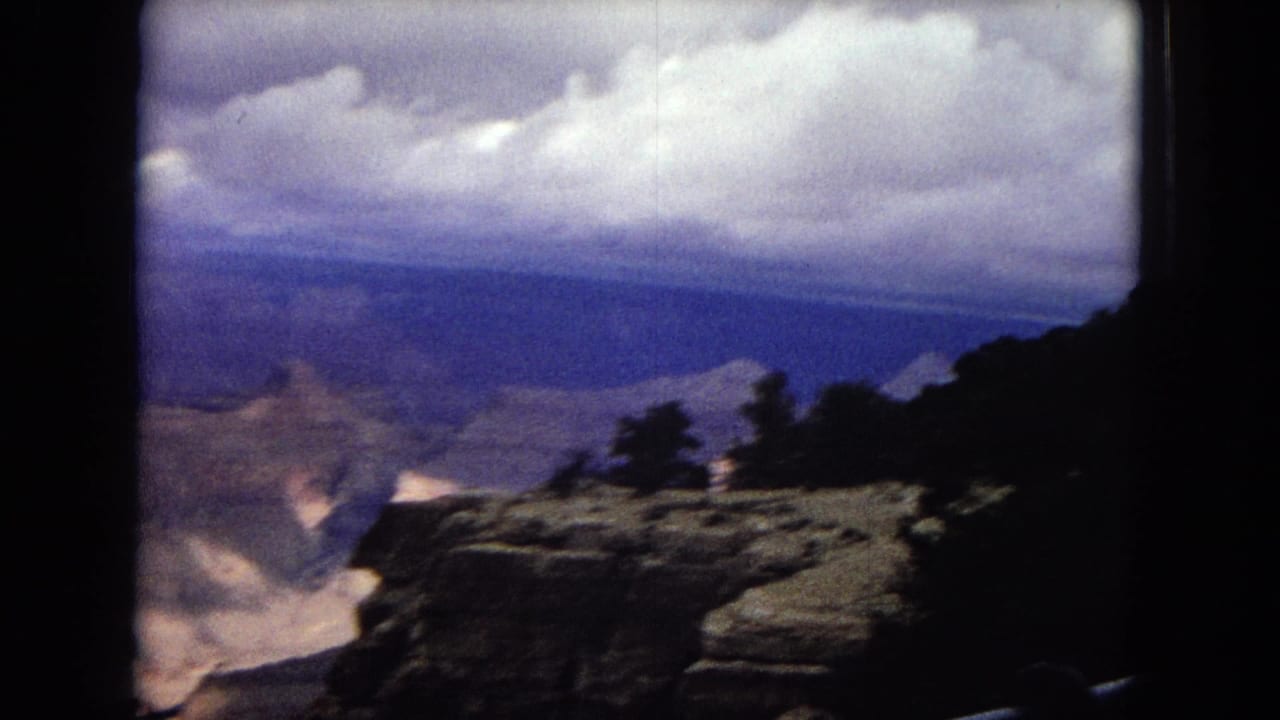 1967 Arizona 8mm frame showing a broad canyon view beneath a cloudy sky, with rocky foreground rim and heavy rounded scan borders.