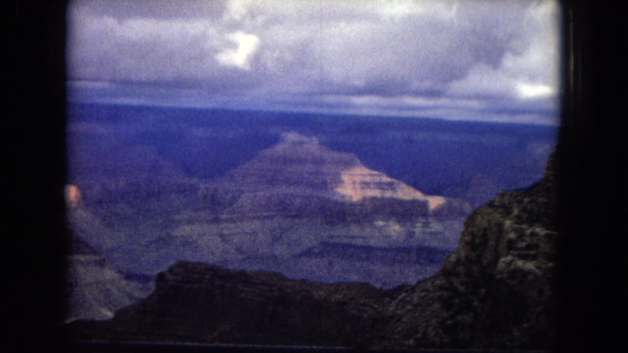 Wide canyon landscape with distant rock formations beneath low clouds.