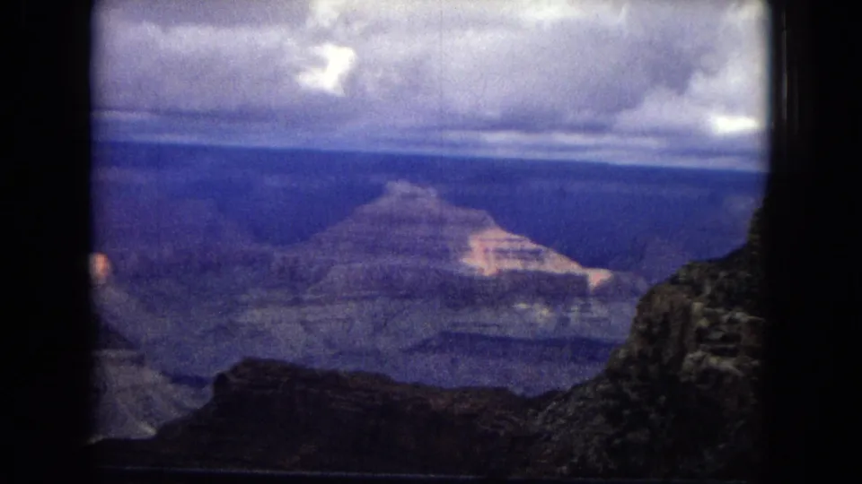 1967 Grand Canyon travel footage frame showing distant mesas and layered rock walls under a broad, overcast sky with aged 8mm color shift.