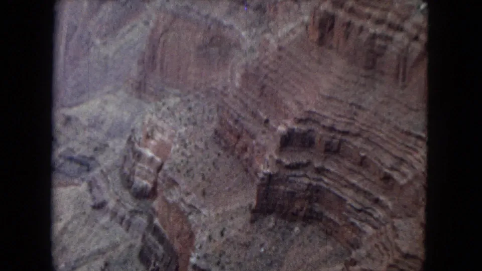 1967 Arizona 8mm frame showing red and tan canyon formations, stepped erosion patterns, pale slopes, and the vertical edge of the film frame.